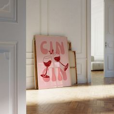 a pink poster with wine glasses on it sitting in front of a white wall and wooden floor