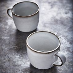 two white coffee mugs sitting on top of a gray counter next to each other