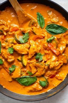 a skillet filled with chicken and spinach covered in orange sauce, garnished with green leaves