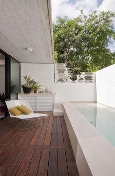 an outdoor swimming pool with wooden floors and white walls, next to a deck that has a lounge chair on it