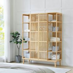 a bamboo shelf with towels on it next to a plant in a white living room