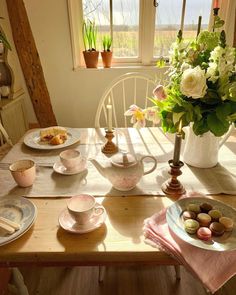 a wooden table topped with plates and cups filled with food next to a vase full of flowers