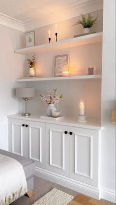 a white shelf with candles and flowers on it in a room that is well lit