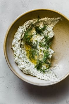 a bowl filled with hummus and dill on top of a white countertop