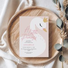 a pink and white swan baby shower card on a wooden plate