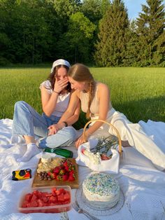 two young women sitting on a blanket in front of a cake and fruit platter