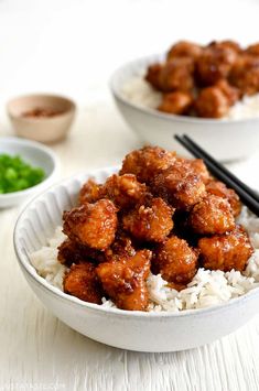 two bowls filled with meat and rice on top of a white table next to chopsticks