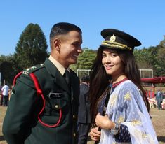 a man in uniform standing next to a woman wearing a white dress and green hat