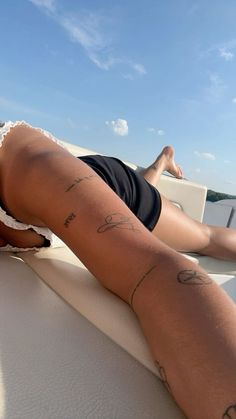 a woman laying on the back of a boat with her legs spread out and tattoos on her leg