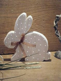 a white wooden bunny with polka dots on it's ears and tail, sitting next to some green stems