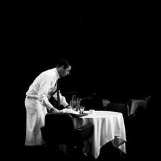 black and white photograph of a man in chef's uniform writing on a table