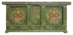 an old green painted cabinet with flowers and words on the front, sitting against a white background