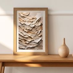 a wooden table topped with a vase next to a framed paper art piece on top of a wall