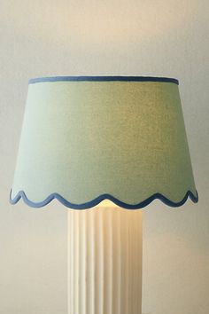 a white lamp with a blue shade on it sitting on a table next to a wall