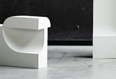 two white chairs sitting next to each other on top of a cement floor in front of a black wall