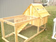 a wooden chicken coop sitting on top of a grass covered field next to a building