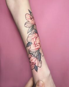 a woman's arm with pink flowers on the left side of her arm and an arrow tattoo on the right forearm