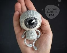 a hand holding a small crocheted doll with an eyeball