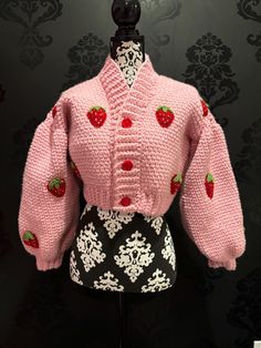 a pink knitted sweater with strawberries on the front and back, sitting on top of a mannequin