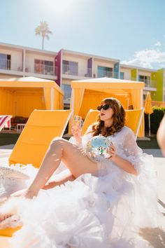 a woman is sitting on the beach with a glass of wine in her hand and wearing sunglasses