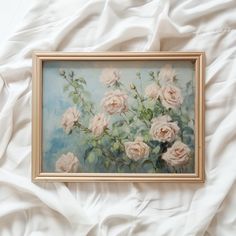 an oil painting of pink roses in a gold frame on a white bed linens