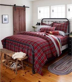 a bed with red and black plaid comforter in a bedroom next to a wooden bench