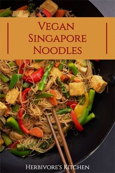 vegan singapore noodles in a wok with chopsticks and vegetables on the side