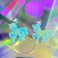 pair of blue and yellow horse shaped earrings on colorful glass surface with multicolored circles in the background