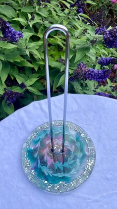 a glass plate with two metal tongs in it on top of a table next to purple flowers