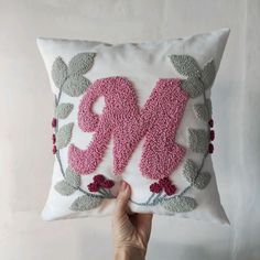 someone is holding up a decorative pillow with the letter m in pink and green on it