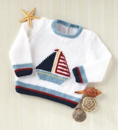 a white sweater with a sailboat on it next to a seashell and starfish