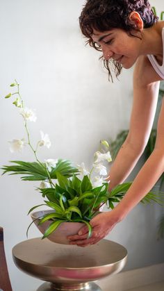 a woman placing flowers in a pot on top of a table