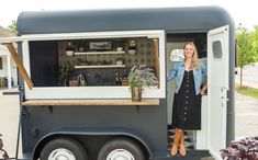 a woman standing in the doorway of a food truck with flowers on it's side