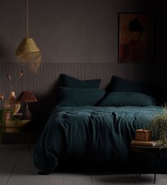 a bed with green sheets and pillows in a dark room next to a painting on the wall