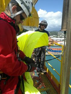 two men in safety gear standing on the side of a boat looking down at something