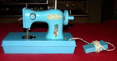 an old blue sewing machine sitting on top of a red carpeted floor next to a box