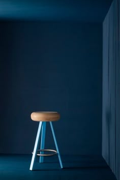 a wooden stool sitting on top of a blue floor next to a white wall in an empty room