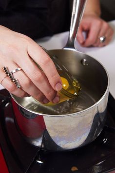 a woman is pouring olives into a saucepan on the stove with her hands