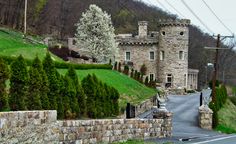 an old stone house on the side of a road in front of a green hillside