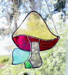 a stained glass lamp hanging from a chain in front of a window with trees behind it