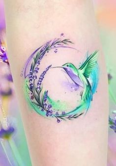 a watercolor tattoo with a humming bird and lavenders on the side of a woman's thigh