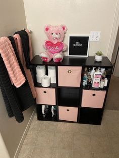 a pink teddy bear sitting on top of a black shelf next to some towels and toilet paper