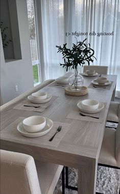 a dining room table with white plates and place settings in front of a large window