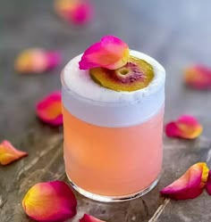 a pink drink with a flower on the top and petals around it, sitting on a table