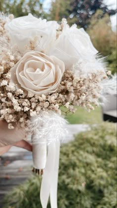 a bridal bouquet with feathers and flowers in someone's hand on the street