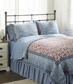 a bed with blue bedspread and pillows in a room next to a window