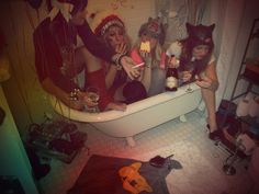 four women dressed up in costumes are sitting in a bathtub and drinking booze