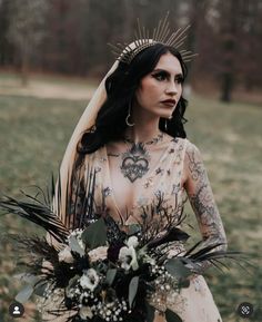 a woman in a wedding dress with tattoos on her body holding a bouquet and looking at the camera