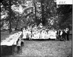 an old black and white photo of a group of people standing in front of a long table