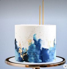 a white and blue cake with gold sprinkles sitting on a metal stand